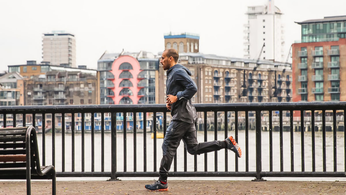 A Male Runner Running Along A Riverwalk In Fall/winter With Warm Clothing On.