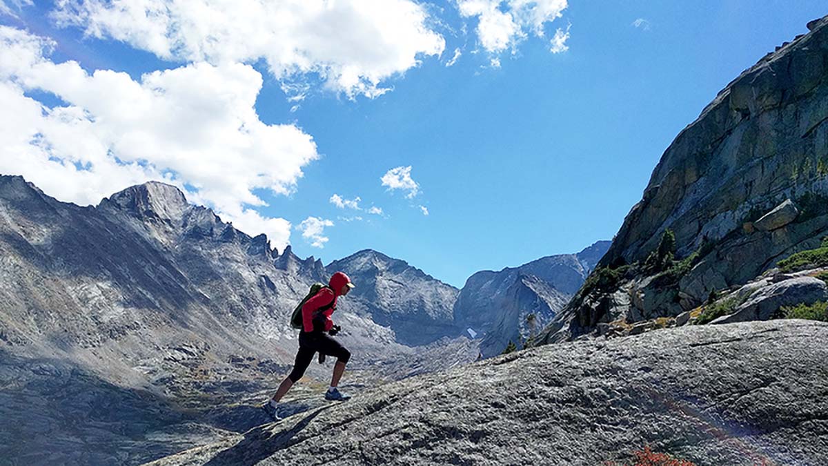 A Trail Runner Climbing A Rocky Surface With A Vast Mountain Valley In The Background