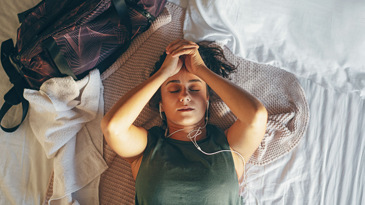 Young Woman After Training Lying On Bed And Listening Music