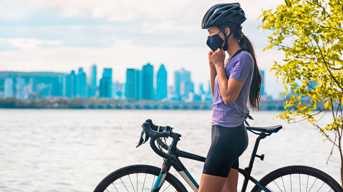 Wearing Covid 19 Mask While Riding Bike. Sport Cyclist Woman Biking Putting On Face Mask For Covid 19 Prevention During Summer Outdoor Leisure Exercise Activity. Fitness Outside.