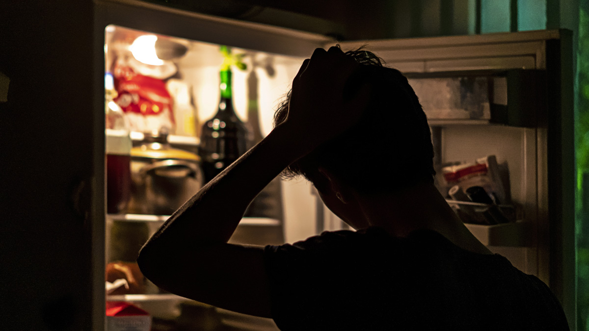 Man Standing Near The Opened Fridge To Pick Some Food At Night At Home