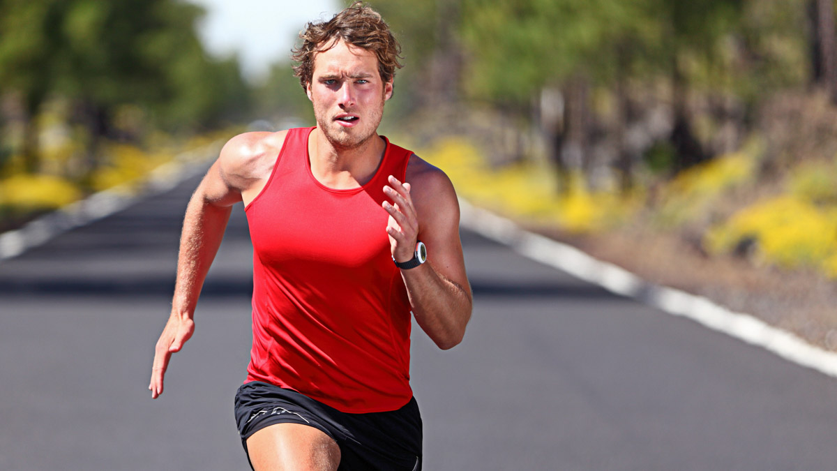Image Of A Male Runner In Red Shirt And Shorts Sprinting Down A Road Doing Burst Training