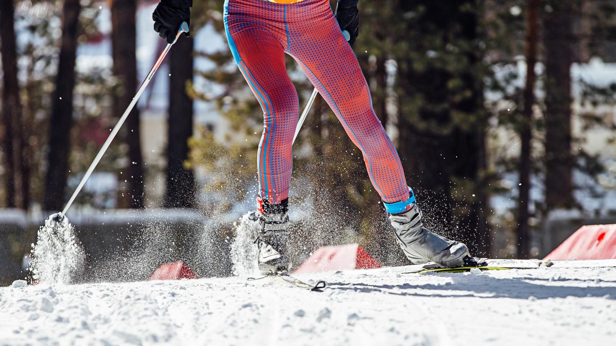 Waist Down Of Cross Country Skier In Pink Pants Skate Skiing In Snow Next To A Forest