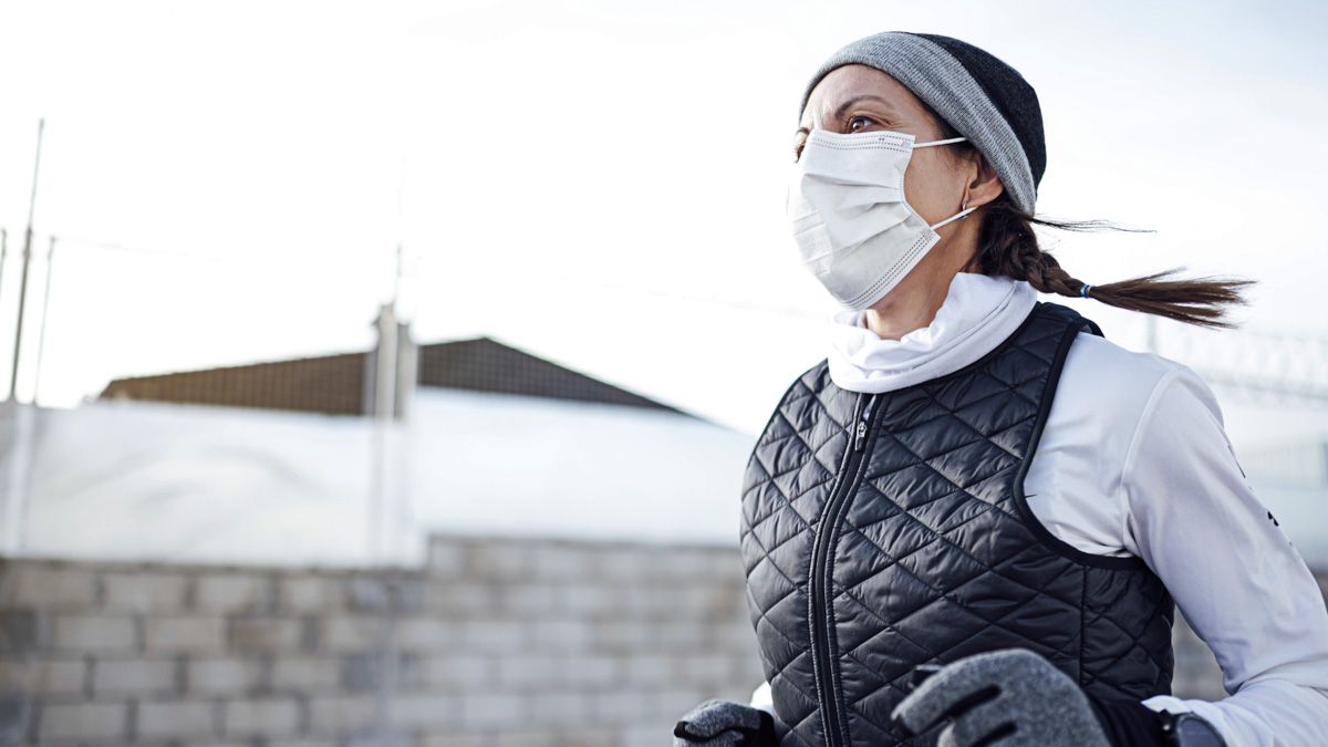 Female Runner Jogs Down Suburban Street In Winter Clothes And Covid Mask