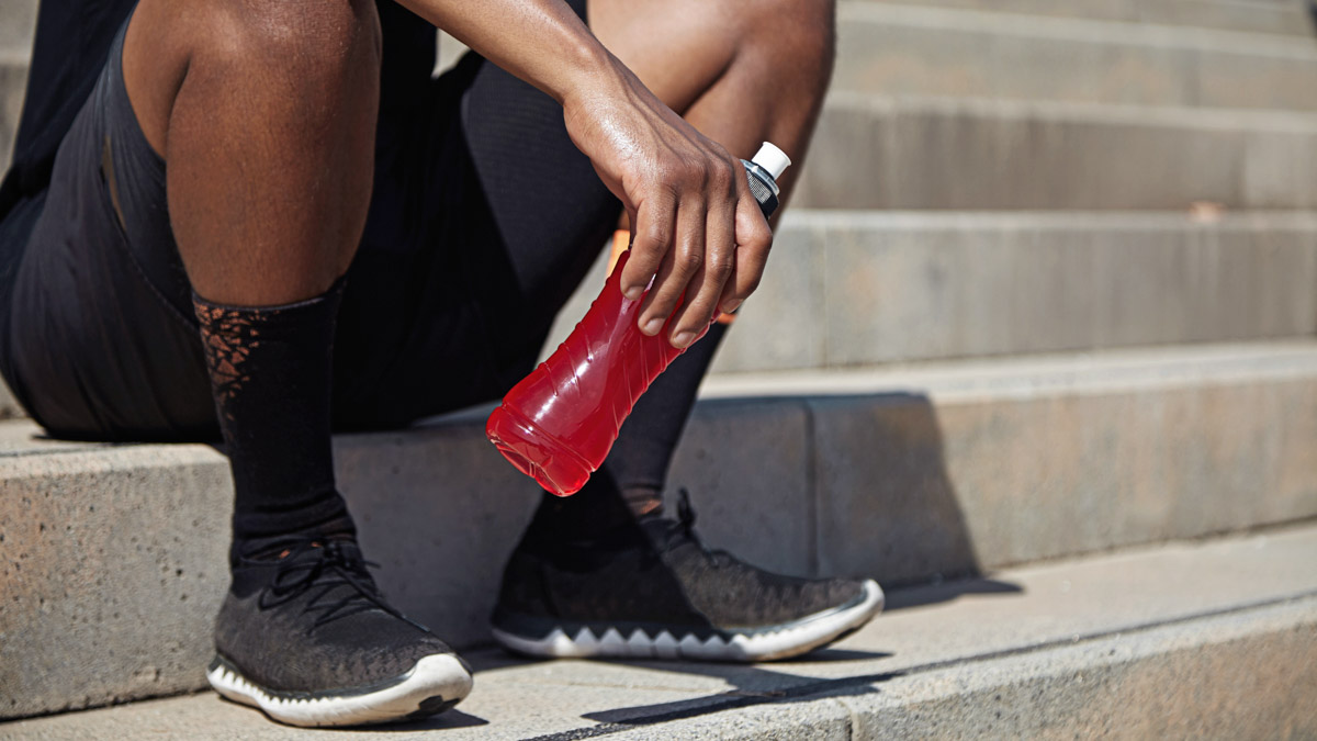 Black Male Runner Sits On City Steps With Red Electrolyte Drink