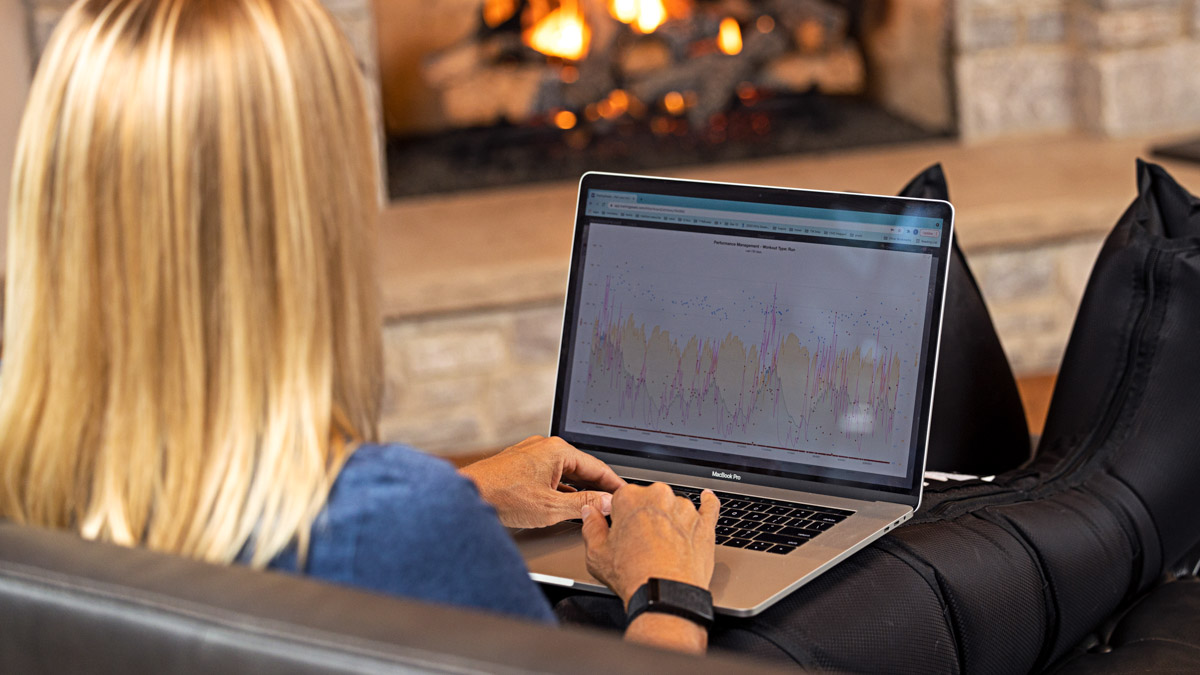 Trainingpeaks Ambassador Uses Sports Tech On Her Laptop In The Living Room In Front Of The Fireplace