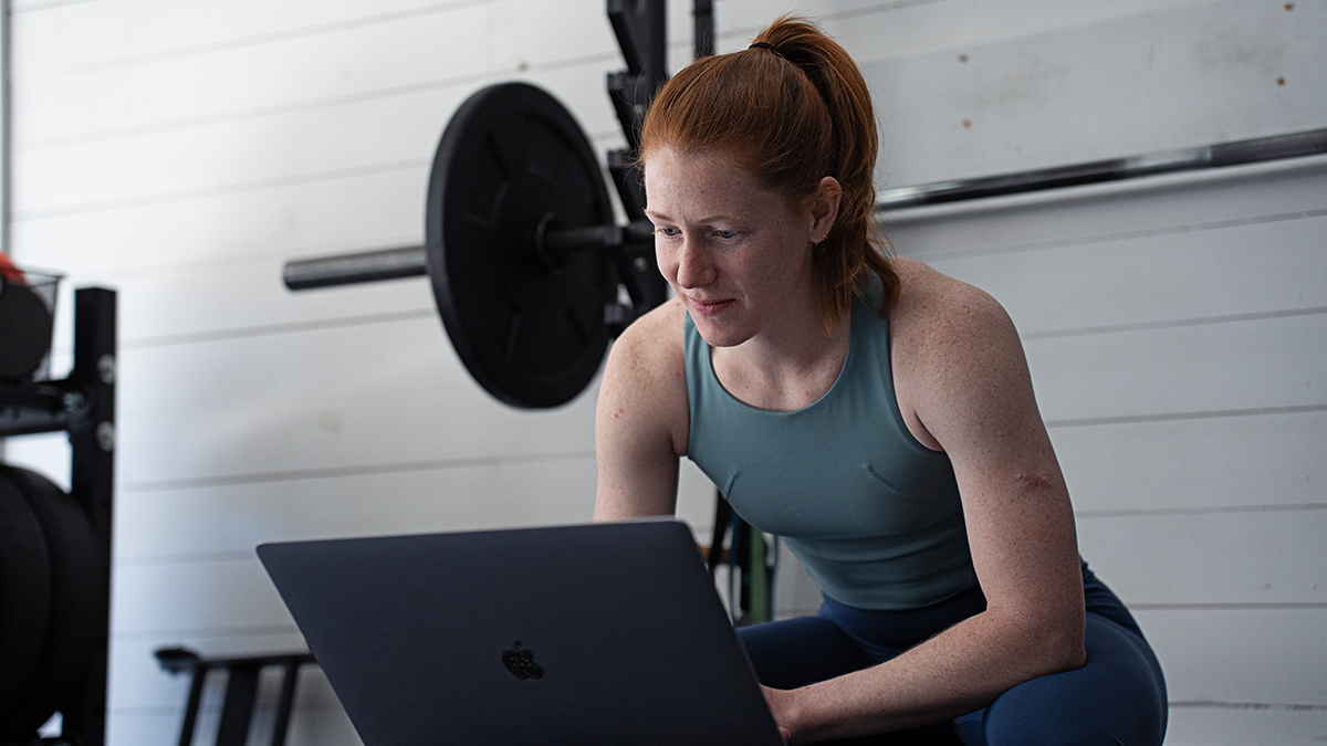 Female Coach Sitting In Gym With Her Laptop Programming Strength Training For Her Endurance Athletes Using Trainingpeaks