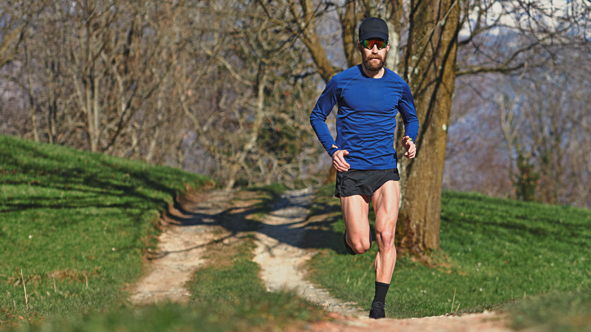 Fit Male Runner Running Down A Dirt Path Through The Woods While Ultramarathon Training