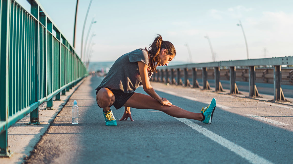 Young Female Runner On Bridge Doing Mobility Exercises To Help With Chronic Pain