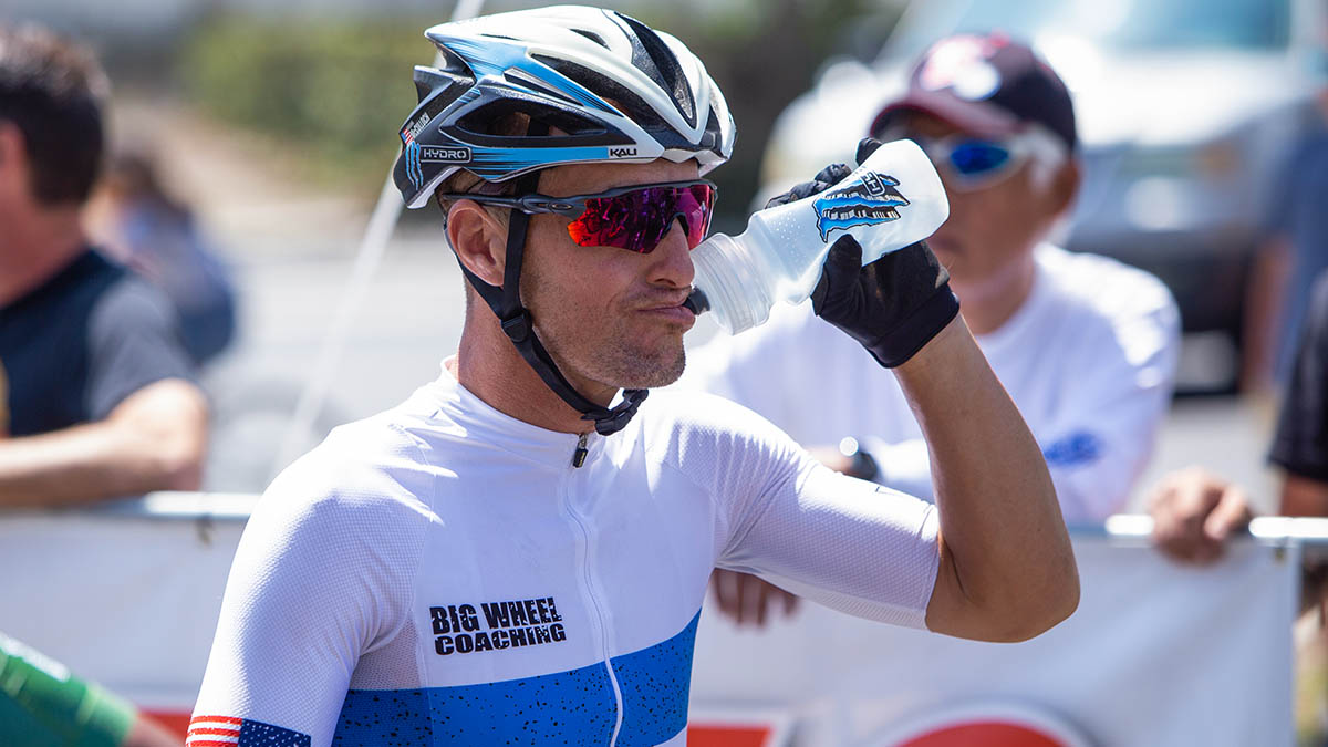 A Male Cyclist At The Start Of A Race Drinking Cold Water Out Of A Bottle In The Heat