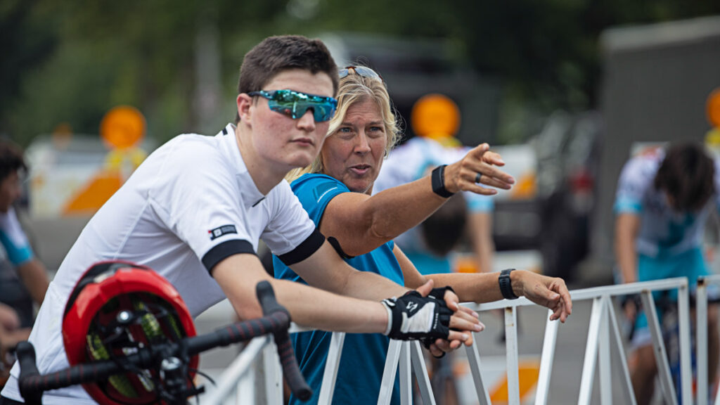 a female coach talking to a male cyclist on the sidelines of a bike race about tactics