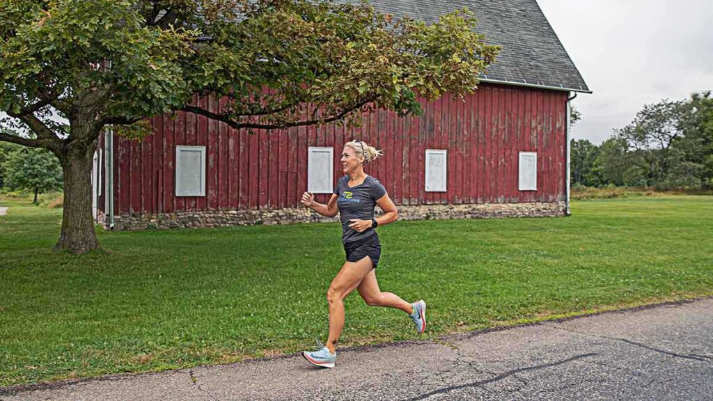a woman running on the road with an old barn in the background