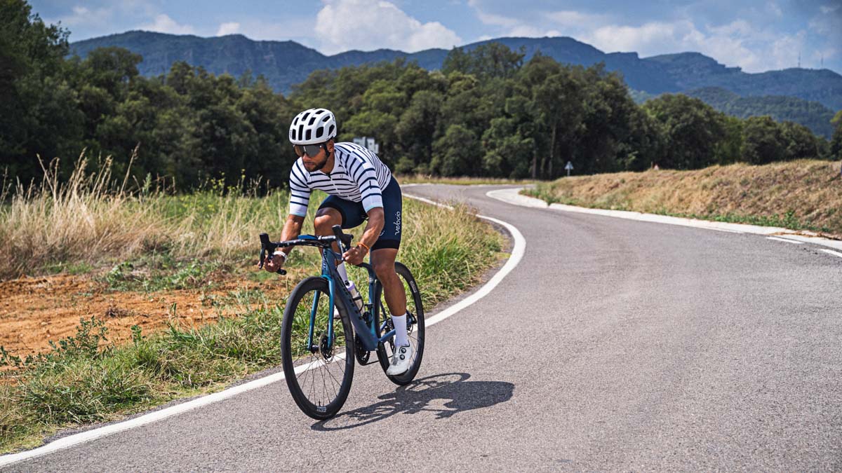 A Fit Cyclist Of Color Riding A Road Bike In The Drops On A Road In The Foothills.