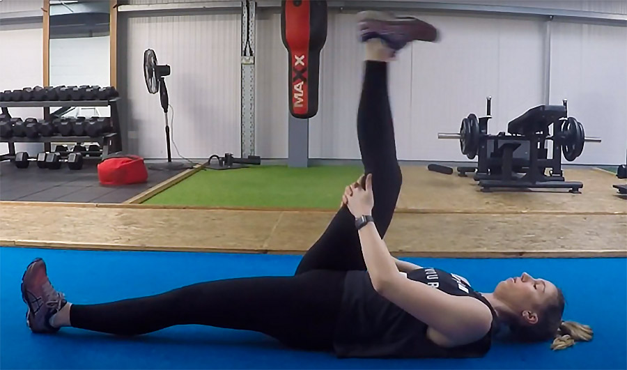 a woman on her back with one leg straight up to measure her posterior chain flexibility. 