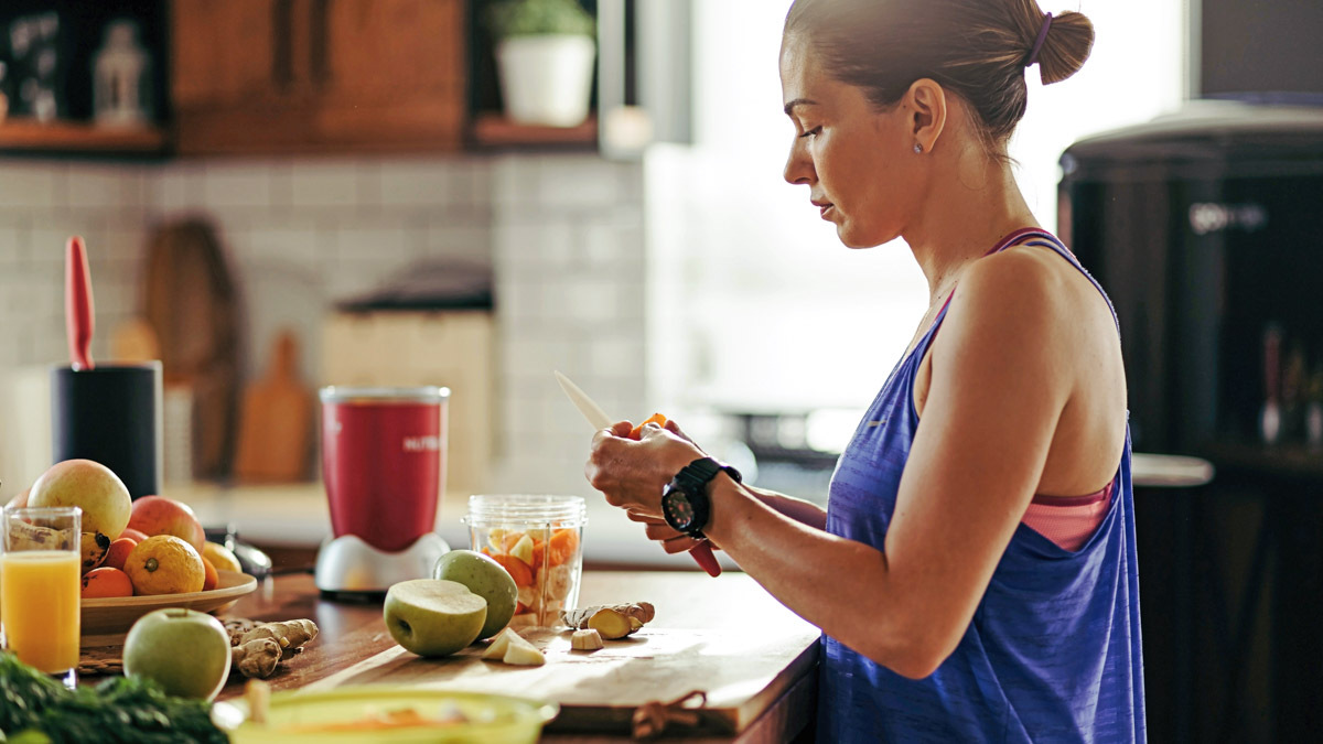 Image Of An Athletic Woman Slicing Fruit While Preparing Smoothie In The Kitchen For Honing In On Her Marathon Nutrition