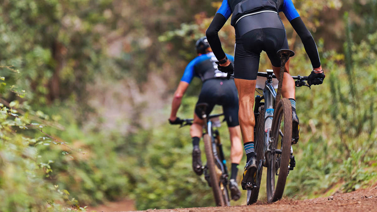 Two Fit Cyclists Ride Down A Dirt Path Training Their Cycling Muscles