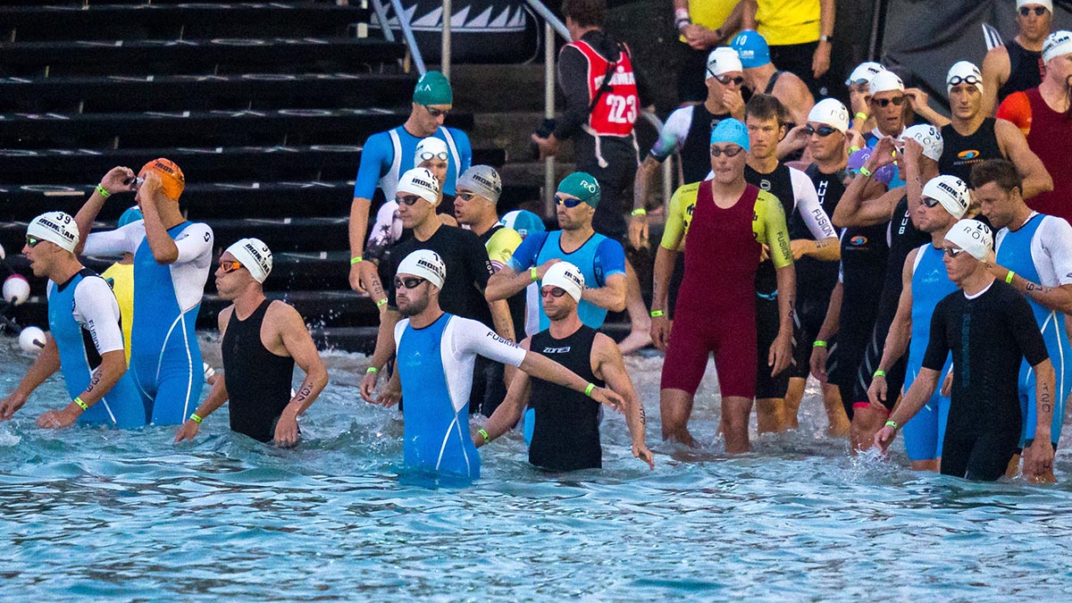 Dozens Of Triathletes Make Their Way Into The Water At The Start Of A Race On The Beach.