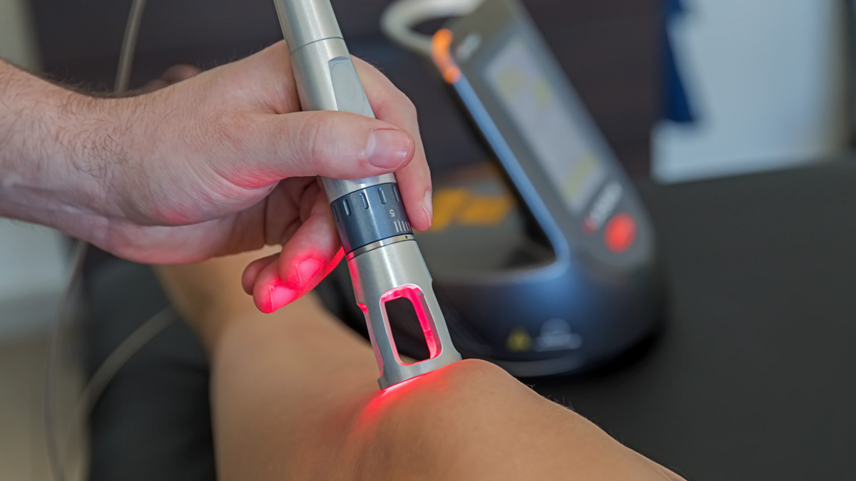 A Technician Using A Laser Therapy Light On A Knee In An Office Setting