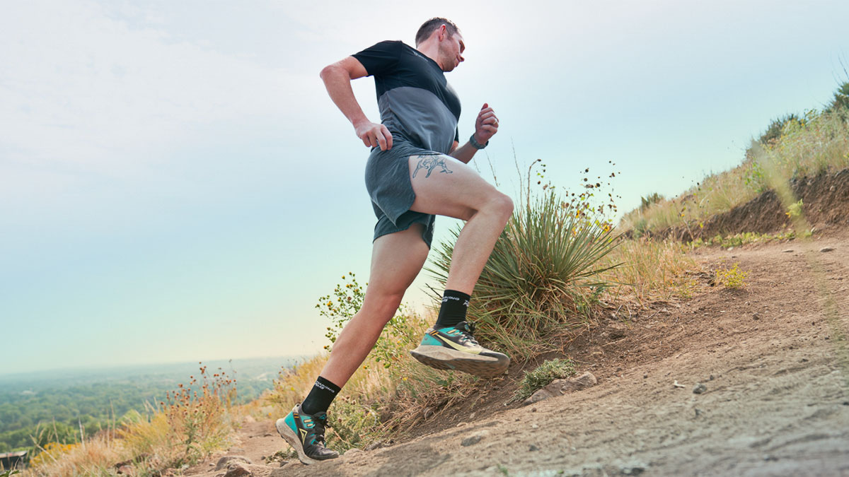 A Man Running Up A Hill On A Trail In Shorts And A Shirt.