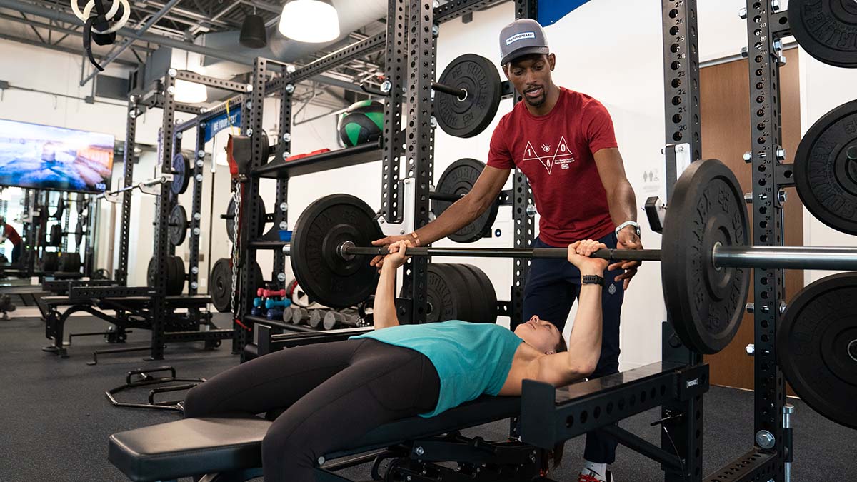 A Coach Working With A Female Athlete In A Weight Gym